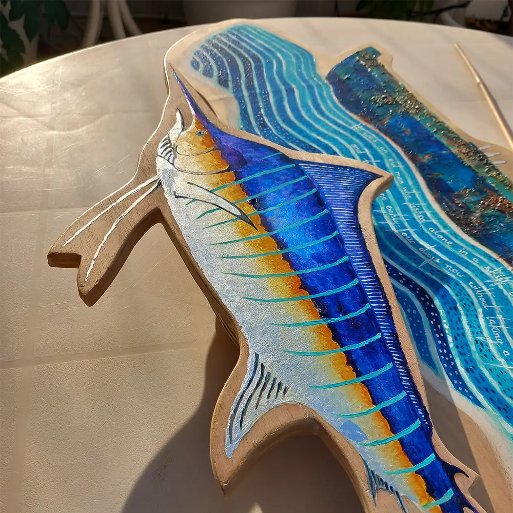 The Old Man and the Sea from Hemingway's novel, depicted in a colorful painting on wood. The old man is in a boat on the sea. A big silver and blue fish is below, seen here in close-up.