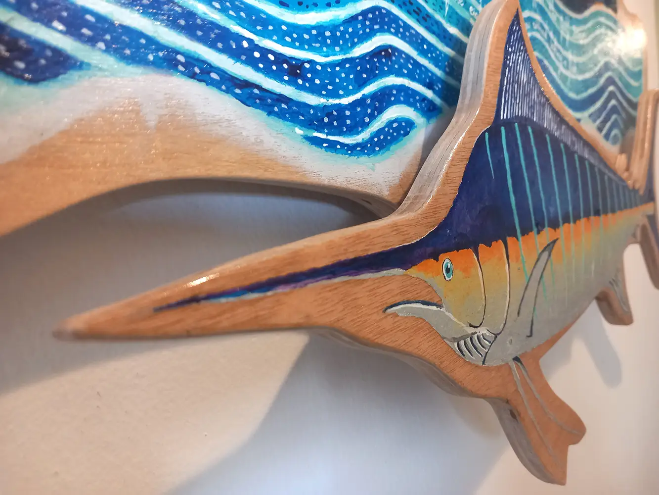 The Old Man and the Sea from Hemingway's novel, depicted in a colorful painting on wood. The old man is in a boat on the sea. A big silver and blue fish is below, seen here in close-up.